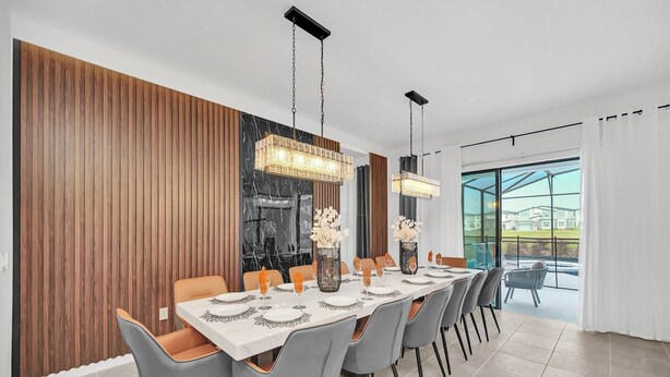 A modern dining area with a long table, grey chairs, and hanging pendant lights. - Last Minute Disney! Private Pool, Hot Tub, Game Room & Themed Bedrooms. Book Now! #113561 (Orlando)