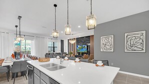 A modern kitchen with a large island, pendant lighting, and artwork on the walls. - Last Minute Disney! Private Pool, Hot Tub, Game Room & Themed Bedrooms. Book Now! #113561 (Orlando)