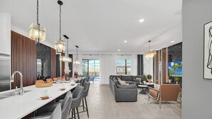 A modern kitchen with a long countertop, bar stools, and pendant lighting. - Last Minute Disney! Private Pool, Hot Tub, Game Room & Themed Bedrooms. Book Now! #113561 (Orlando)