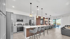 A modern kitchen with a central island, stainless steel appliances, and a dining area with grey chairs. - Last Minute Disney! Private Pool, Hot Tub, Game Room & Themed Bedrooms. Book Now! #113561 (Orlando)