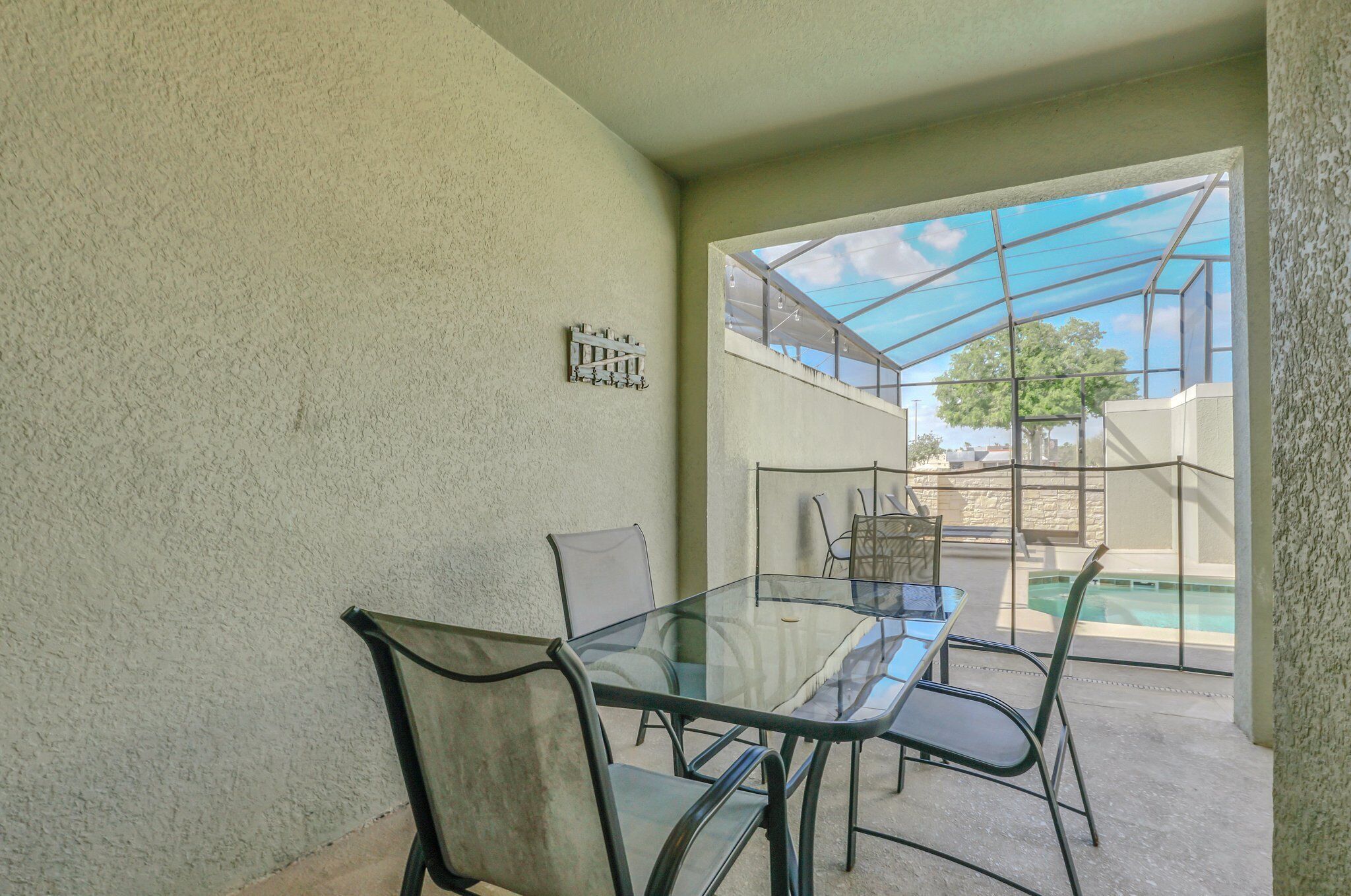 A glass-top table with chairs in a covered outdoor area with a view of a swimming pool.