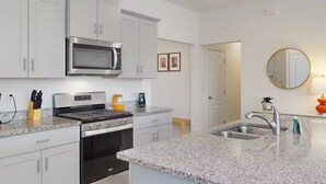 Eine moderne Küche mit weißen Schränken, Edelstahlgeräten, Granit Arbeitsplatten und einer großen Kochinsel mit Spüle.