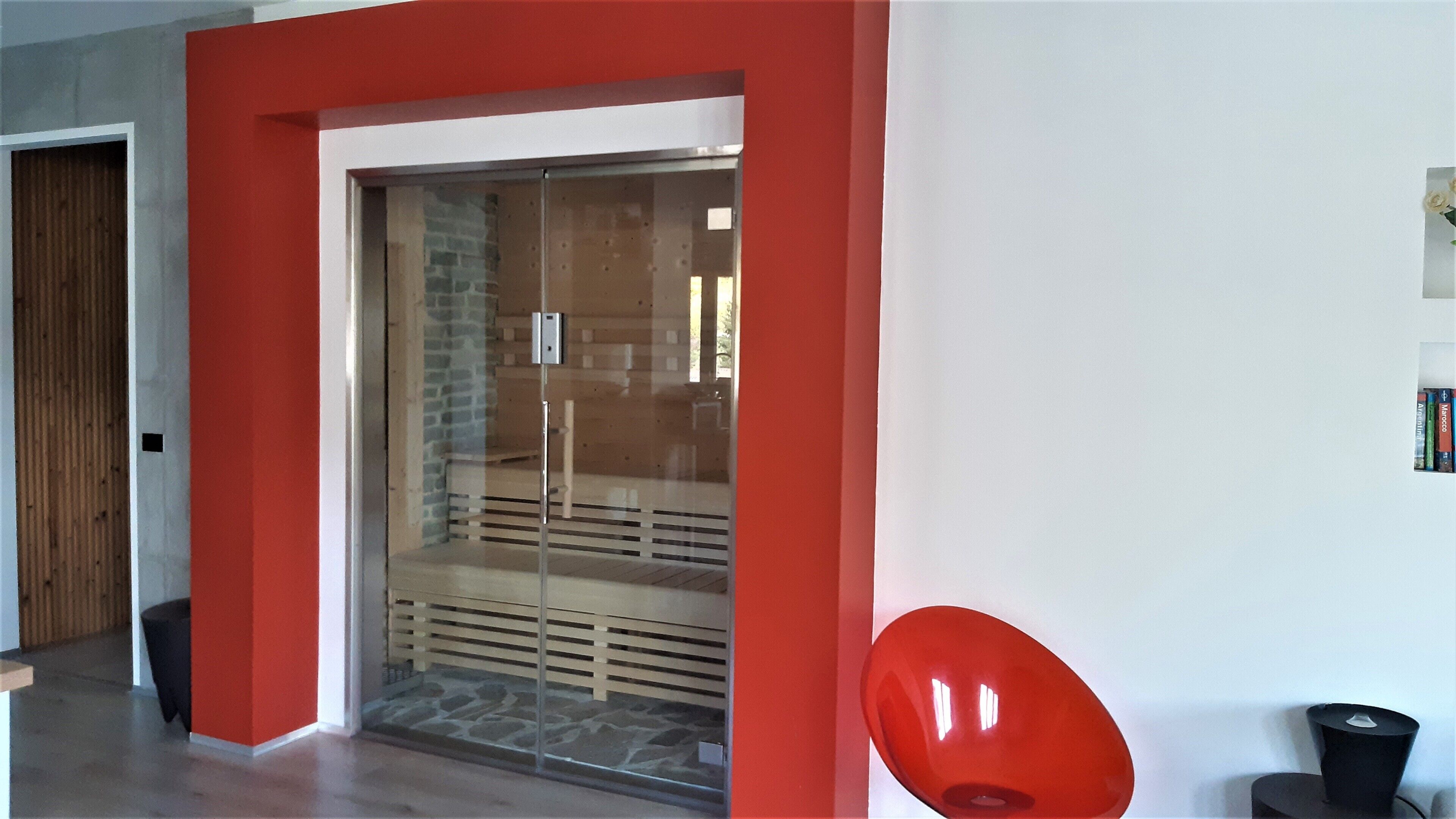 A modern interior with a red accent wall, a glass door leading to a room with a stone wall, and a red chair.