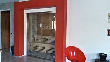 A modern interior with a red accent wall, a glass door leading to a room with a stone wall, and a red chair.