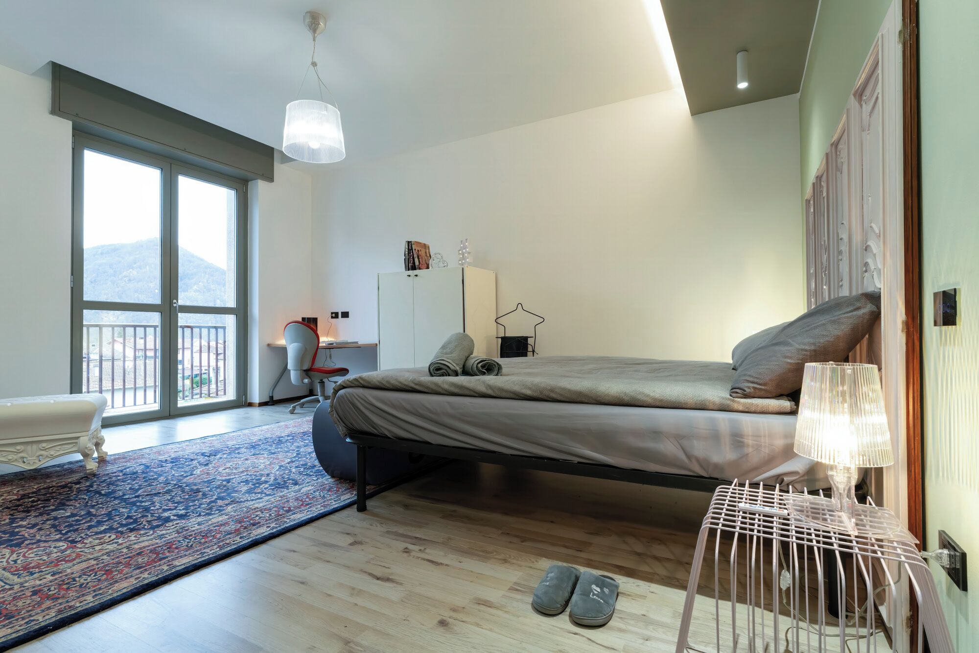 Een moderne slaapkamer met een bed, een bureau en een stoel. Een groot raam biedt uitzicht op het omliggende landschap.