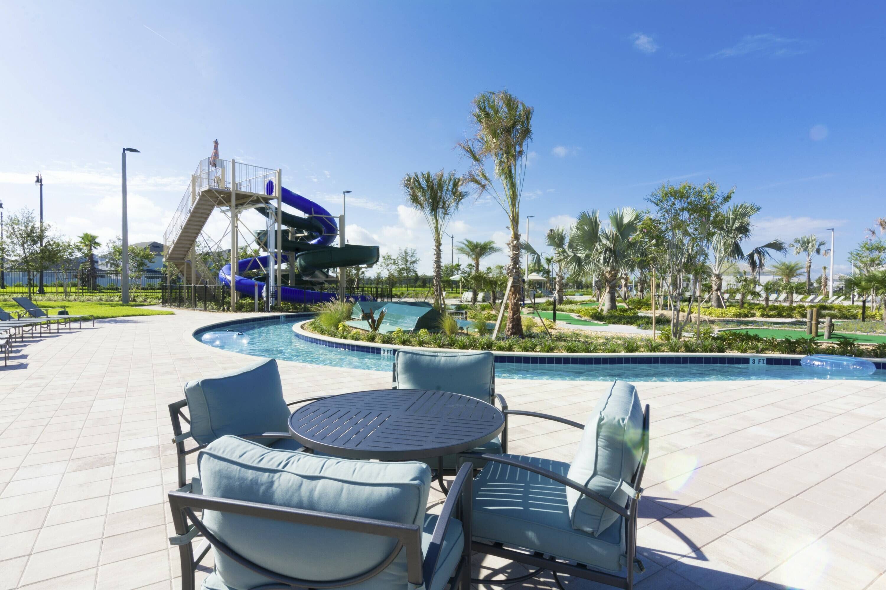 A pool area with a blue water slide, lounge chairs, and palm trees.
