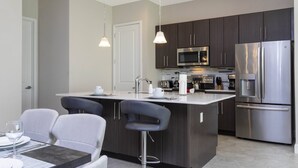 A modern kitchen with dark cabinets, stainless steel appliances, and a central island with bar stools. - Disney! Private Pool, Hot Tub & Themed Bedrooms. Book Now! #VDR14 (Orlando)