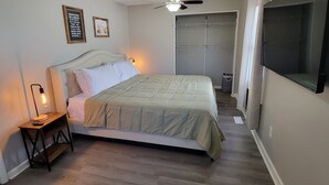 A bedroom with a bed, a nightstand, a ceiling fan, a closet, and a TV mounted on the wall.