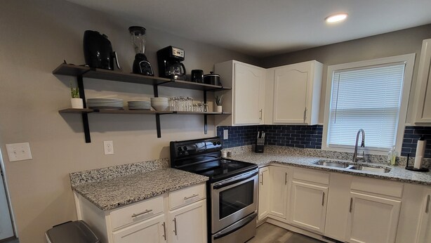 A modern kitchen with white cabinets, a granite countertop, a black stove, and a window with blinds.