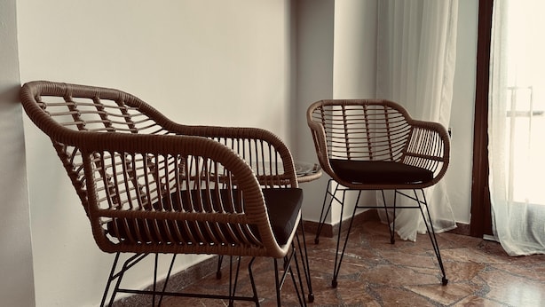 Two wicker chairs with metal frames, positioned near a window with sheer curtains. - Apartment in the Heart of Tinos Town for 4 Guests (Tinos)