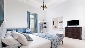 A modern bedroom with a large bed, a dresser, a television, and a bathroom visible in the background. - Grace Suites (Sorrento)