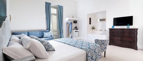 A modern bedroom with a large bed, a dresser, a television, and a bathroom visible in the background.