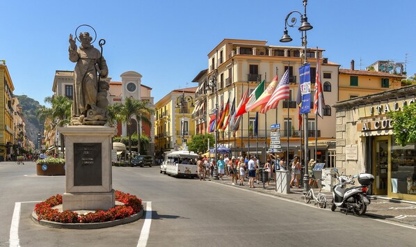 A street scene with a statue, flags, and buildings. - Grace Suites (Sorrento)