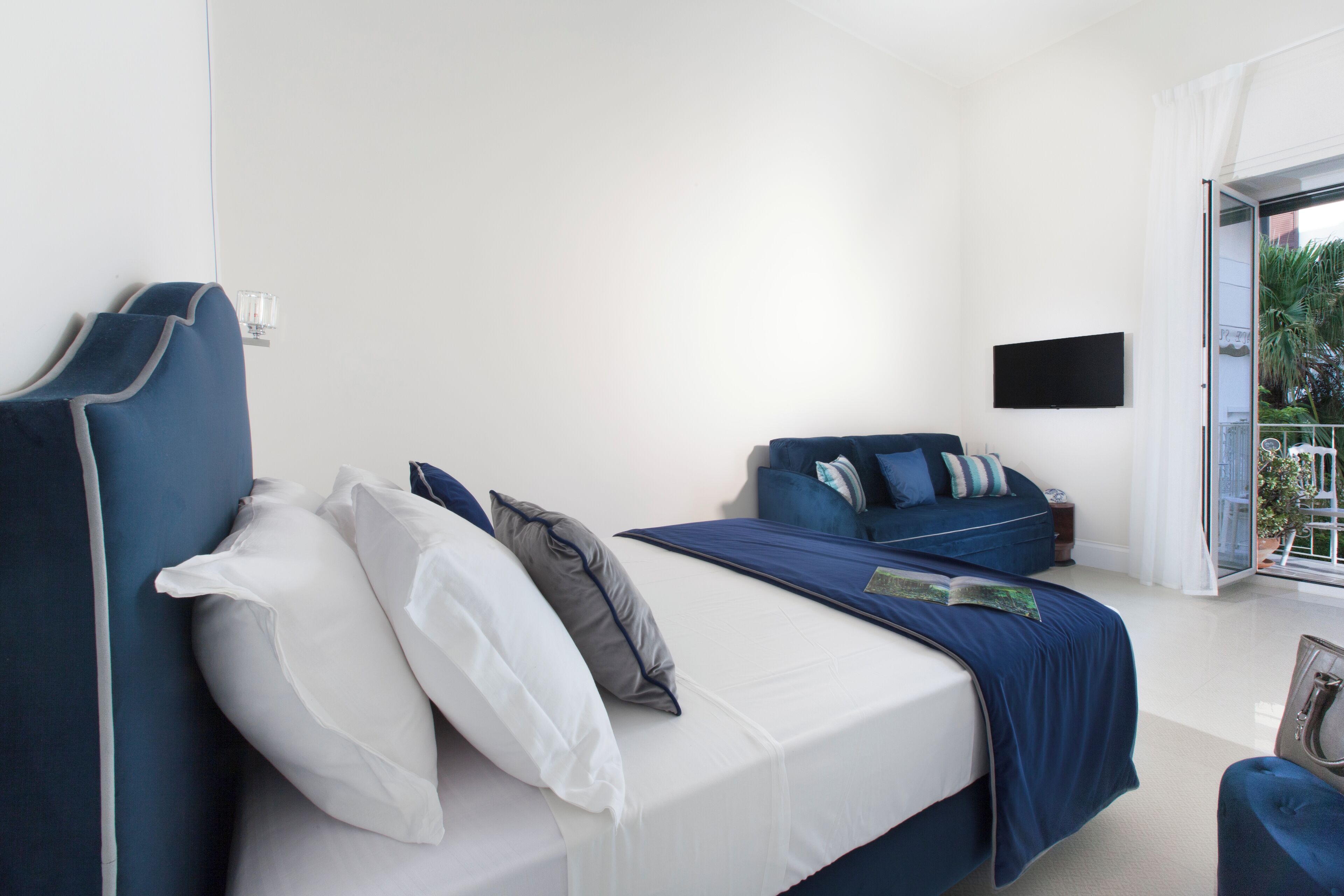 Een slaapkamer met een bed, een bank, een televisie en een balkon.