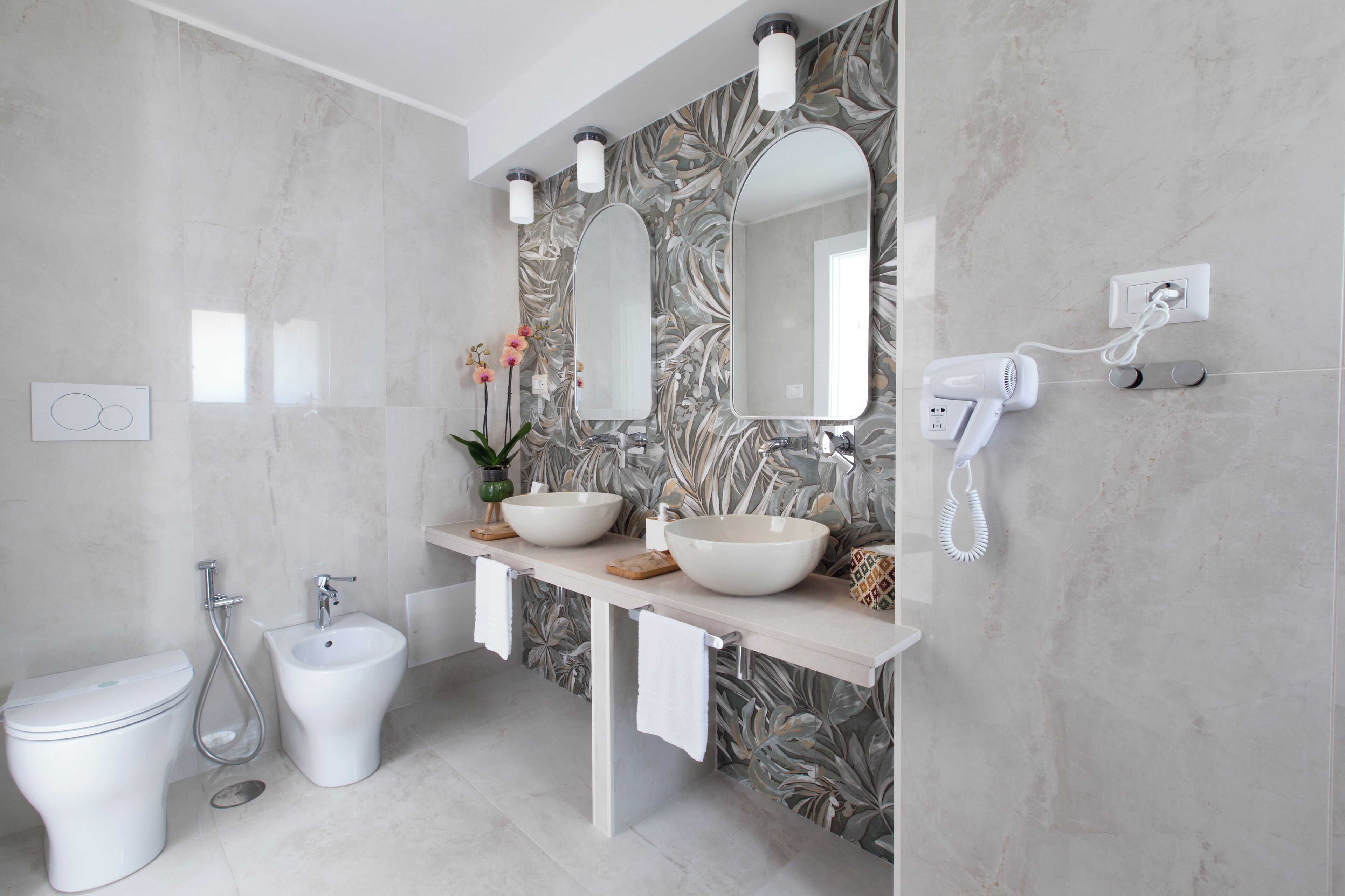 Ein Badezimmer mit Toilette, Bidet, zwei Waschbecken, einem Spiegel und einem Föhn.