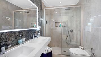 Un baño moderno con un espejo grande, un lavabo blanco, cabina de ducha y un inodoro.