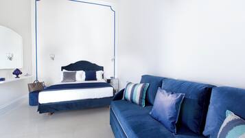 Een slaapkamer met een groot bed, een blauwe bank en een nachtkastje met een lamp.