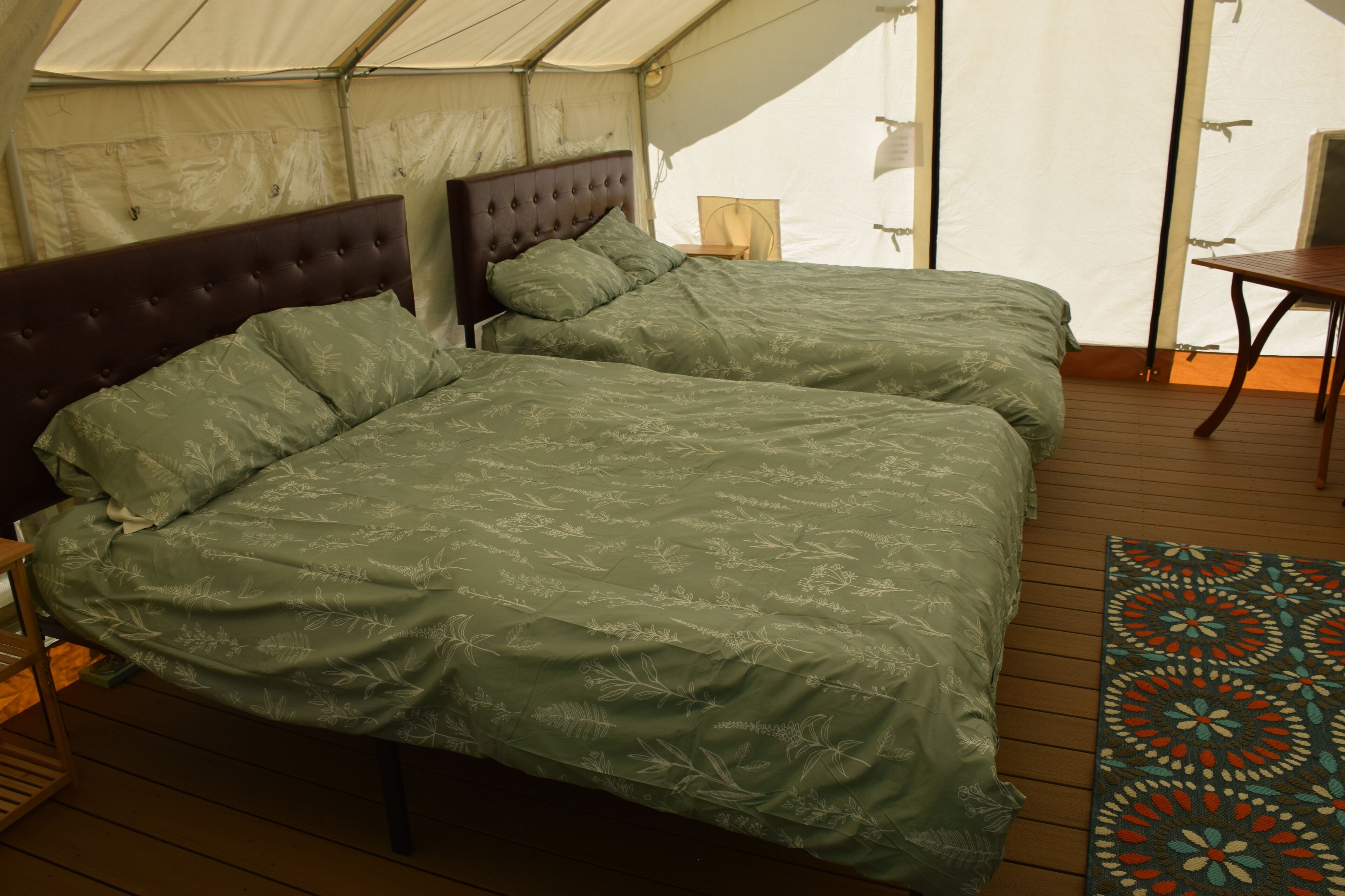 A tent with two beds, each with a headboard and pillows, and a wooden floor.