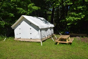 A white tent with a pitched roof, a picnic table, and a blue container nearby. - Peyper Fields Creekside Camp (Newark Valley)
