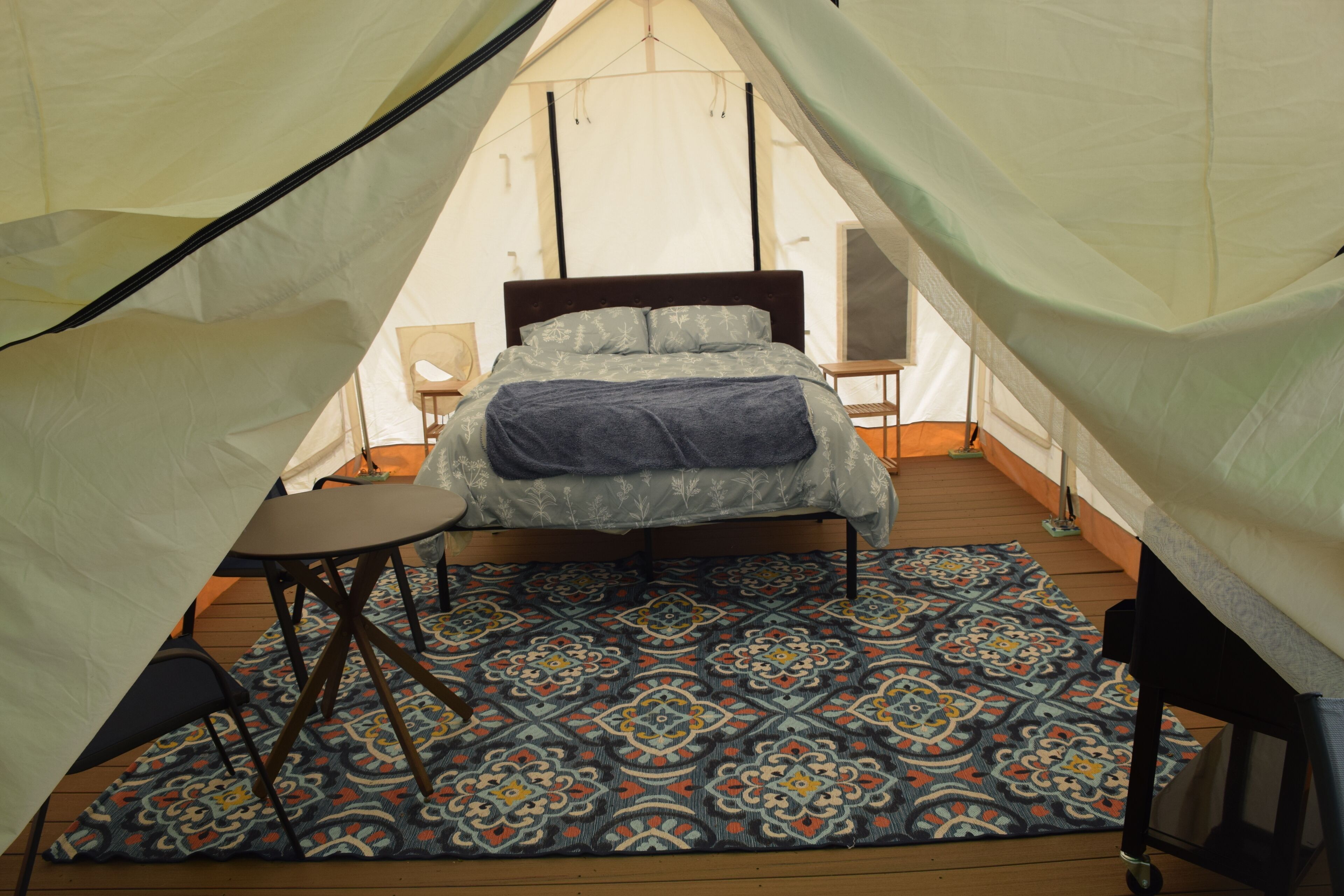 A tented accommodation with a bed, a small table, and a patterned rug.