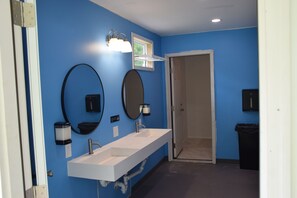 A bathroom with blue walls, a white sink, two mirrors, and a door leading to another room. - Peyper Fields Creekside Camp (Newark Valley)