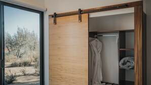 A room with a sliding door leading to an outdoor area, a wooden wardrobe, and a rack with a robe and pillow. - Cabins by 7 Valles (Valle de Guadalupe)