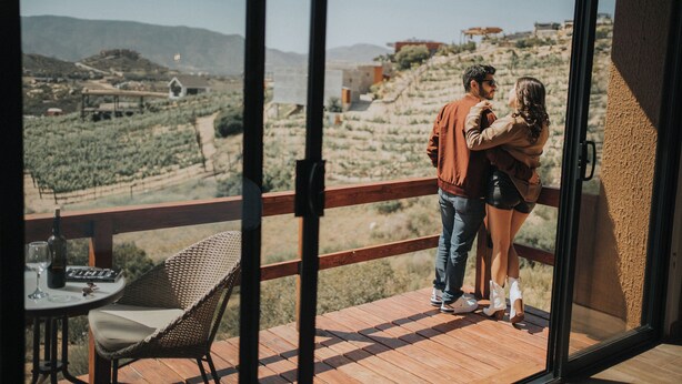 A couple on a balcony overlooking a vineyard. - Cabins by 7 Valles (Valle de Guadalupe)