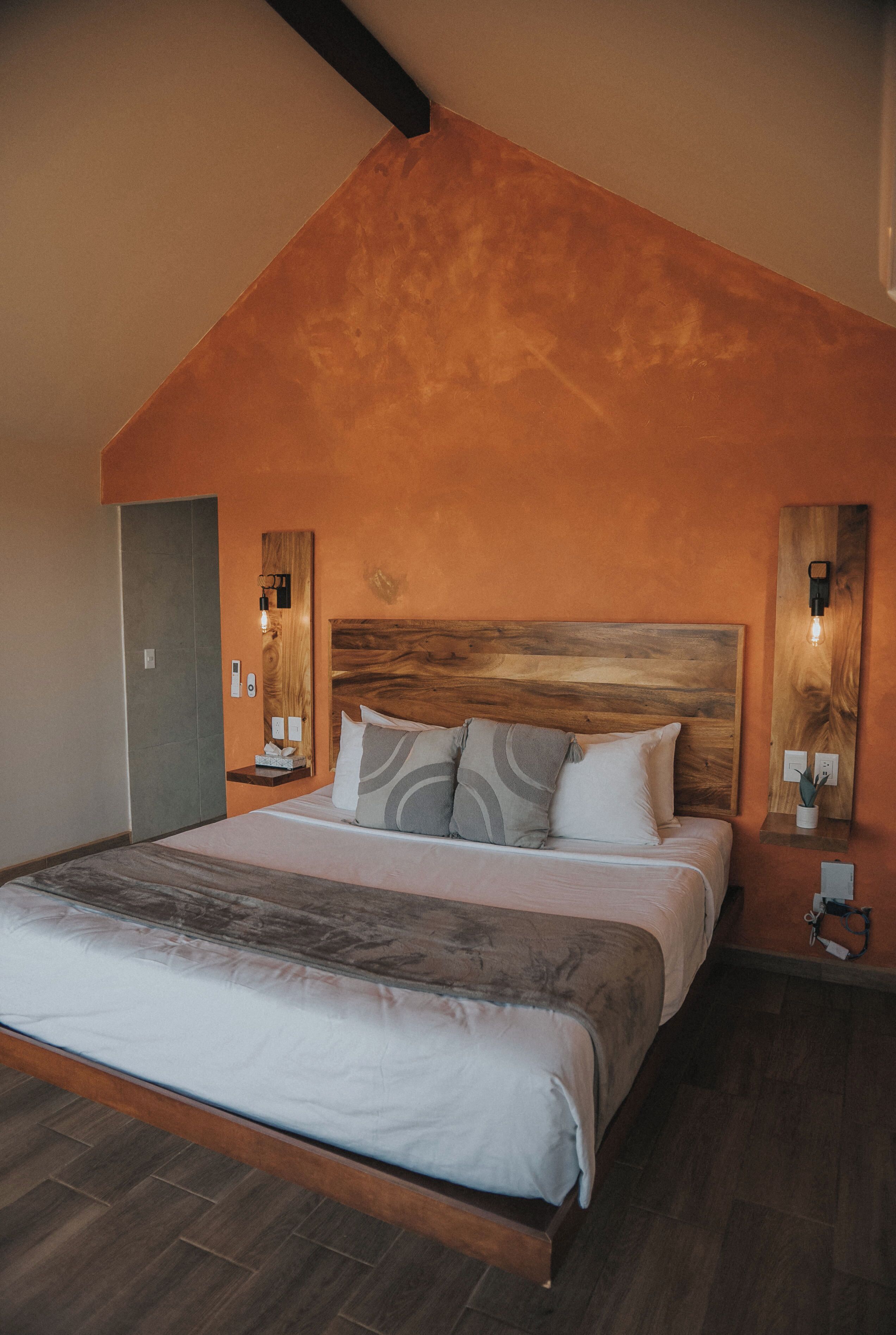 A bedroom with a sloped ceiling, a wooden headboard, a large bed with multiple pillows, bedside tables with lamps, and a wall-mounted light fixture.