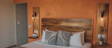 A bedroom with a sloped ceiling, a wooden headboard, a large bed with multiple pillows, bedside tables with lamps, and a wall-mounted light fixture.