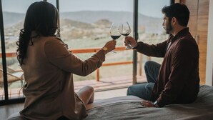 Two people sitting on a bed facing a large window with a view of a landscape. - Cabins by 7 Valles (Valle de Guadalupe)