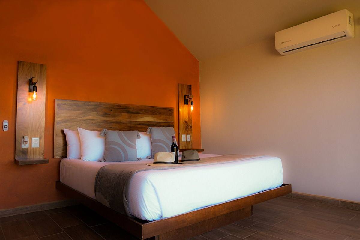 Ein Schlafzimmer mit einem Holz-Kopfteil, einem Bett mit weißer Bettwäsche, zwei Wandleuchten und einer Klimaanlage.