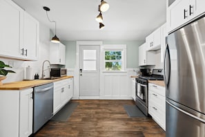 A modern kitchen with white cabinetry, stainless steel appliances, and a wooden countertop. - New! Cozy 2BR near Lake at Anchor Bay (New Baltimore,)