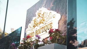 A sign with the words "R. R. Boutique" in gold lettering on a white background, surrounded by flowers. - Hotel Ruko Boutique (Golem)