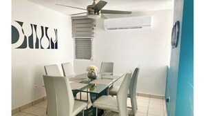Un espace repas moderne avec une table en verre, six chaises, un ventilateur de plafond et un appareil de climatisation.