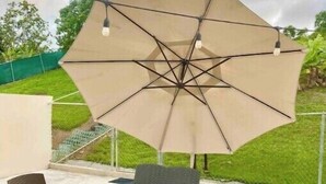 Une terrasse extérieure avec un grand parasol beige, deux chaises, une petite table ronde et un pot de fleurs.