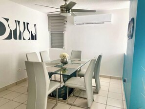 Uma sala de jantar moderna com mesa de vidro, seis cadeiras, ventilador de teto e ar condicionado.