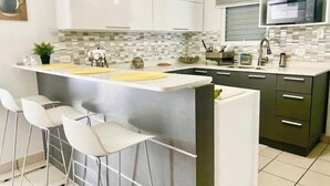 Une cuisine moderne avec des meubles blancs et foncés, un îlot central doté de tabourets et un four à micro-ondes posé sur le plan de travail.