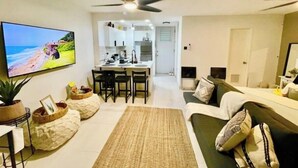 A modern living room with a flat-screen TV, a sofa, a coffee table, and a dining area with a kitchen in the background.
