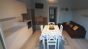 En kompakt opholdsstue med et spisebord dækket til to personer, en sofa med puder, et ophængt fjernsyn og en cykel som pynt på væggen.