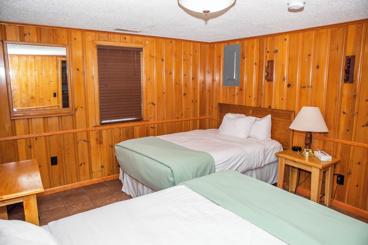 Ein Zimmer mit Holzwandverkleidung, zwei Betten, einer Bank und einem Nachttisch mit Lampe.