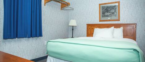 Habitación de hotel con cama, escritorio, lámpara, un cuadro en la pared y una cortina azul.