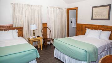 Une chambre d’hôtel avec deux lits, une table de chevet en bois avec une lampe, une chaise et une porte donnant sur une salle de bain.