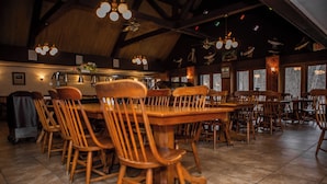 A spacious dining area with wooden tables and chairs, a high ceiling with exposed beams, and large windows with views of the outdoors. - Montauk Lodge (Salem)