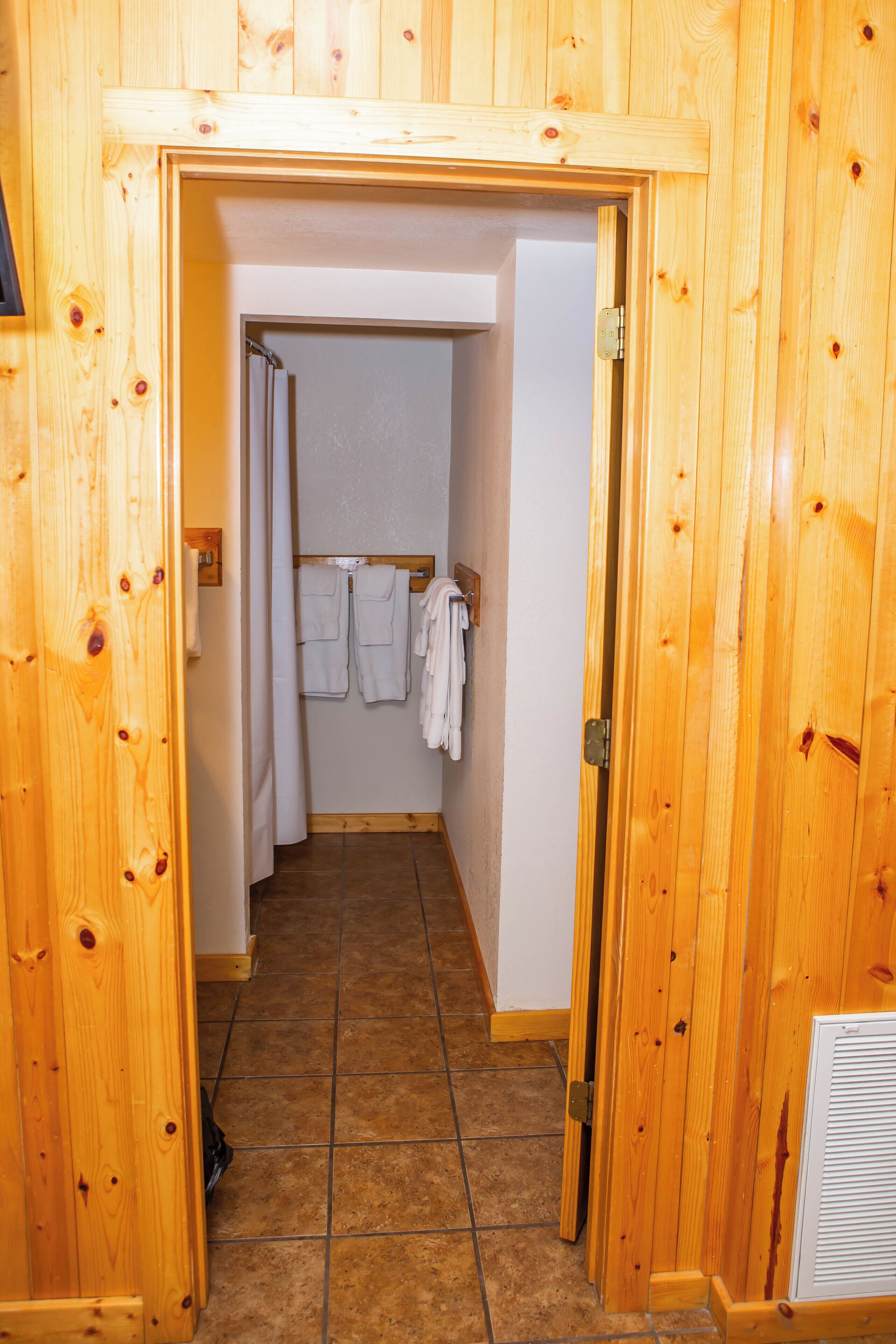 A wooden interior hallway leading to a bathroom with a shower, a towel rack with towels, and a vent on the wall.