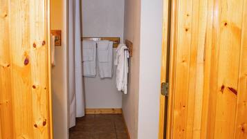 A wooden interior hallway leading to a bathroom with a shower, a towel rack with towels, and a vent on the wall.