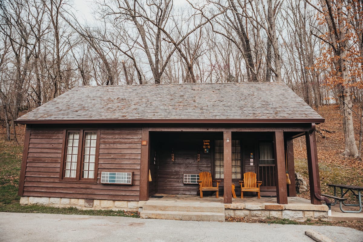 Ein rustikales Blockhaus mit Veranda, zwei Holzstühlen und einem Picknicktisch.