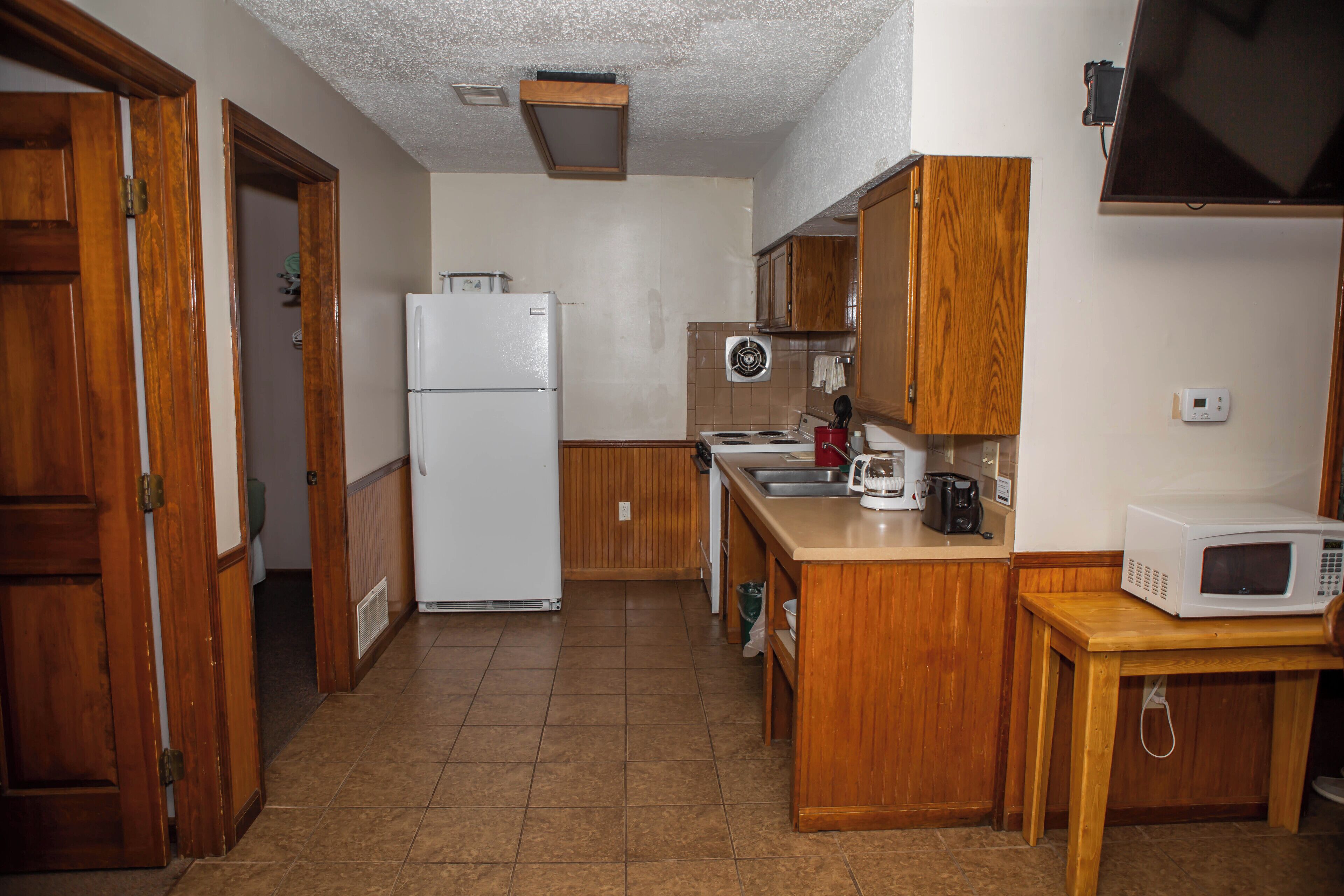 A compact kitchen with wooden cabinets, a white refrigerator, a microwave, and a stove.