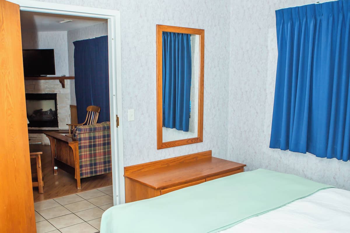 Ein Hotelzimmer mit einem Bett, einem Nachttisch aus Holz, einem Spiegel und Blick auf einen Wohnbereich mit Fernseher und Sitzgelegenheiten.