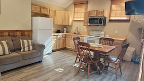A compact kitchen with wooden cabinets, a refrigerator, microwave, stove, and a dining area with a table and chairs. - Montauk Lodge (Salem)