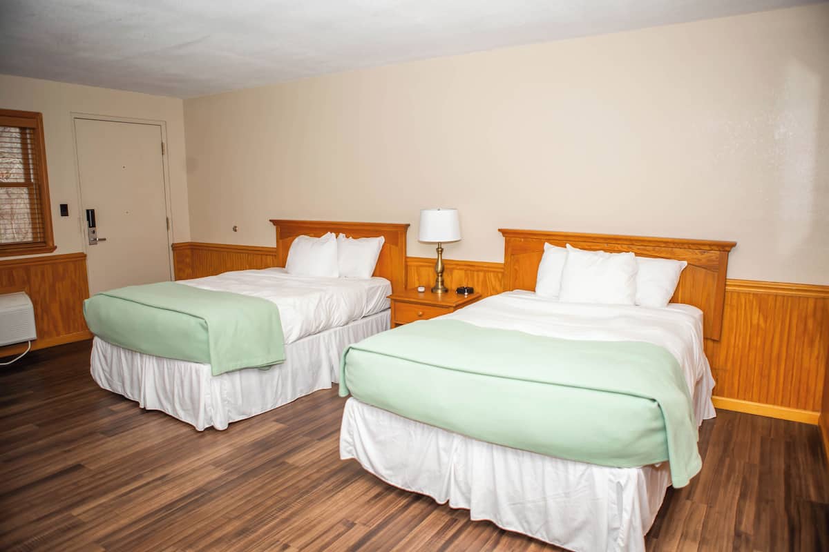 Ein Hotelzimmer mit zwei Betten, Holz-Kopfteilen, einem Nachttisch und einer Lampe.